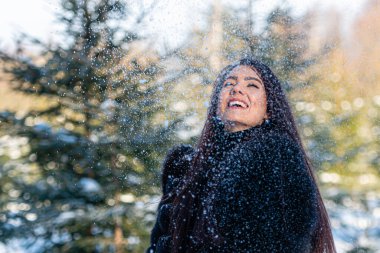 Sıcak kürklü neşeli genç kadın karlı ormanda kış gününün tadını çıkarıyor.