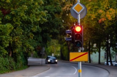 Sonbahar şehrinin odaksız arka planında kırmızı ışığı olan trafik semaforu, yakın plan