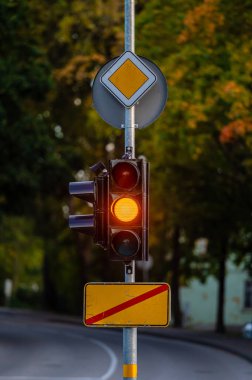 Sonbahar şehrinin arka planında sarı ışığı olan trafik semaforu, yakın plan.