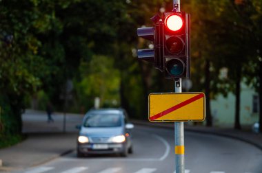 Sonbahar şehrinin odaksız arka planında kırmızı ışığı olan trafik semaforu, yakın plan