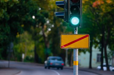 Sonbahar şehrinin kapanmış arka planına yeşil ışık yakılmış trafik semaforu, yakın plan