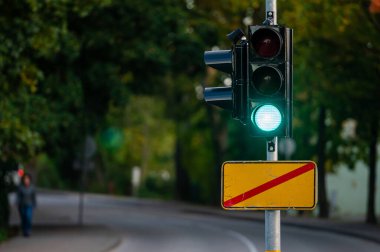 Sonbahar şehrinin kapanmış arka planına yeşil ışık yakılmış trafik semaforu, yakın plan