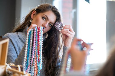 Aynada farklı takıları seçen ve deneyen bir kadının yansıması, yumuşak odak, yakın plan