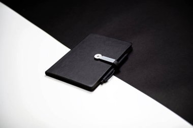 black planner or notebook with pen on two-color black and white background, mockup, copy space