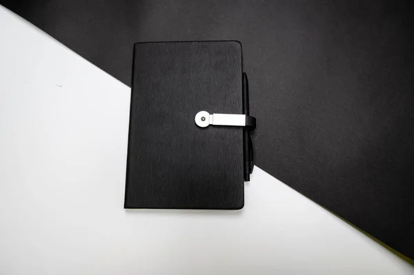 black planner or notebook with pen on two-color black and white background, mockup, copy space