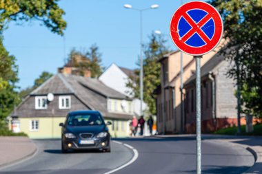 Önünde yol tabelası olan küçük bir kasaba caddesi manzarası ve arka planda trafiği dağıtan