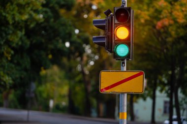 Sonbahar şehrinin odaksız arka planında yeşil ve turuncu ışıklı trafik semaforu, yakın plan