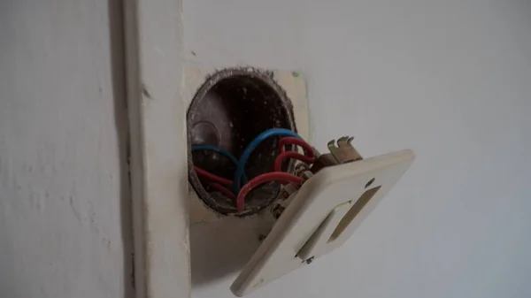 Трехлуночная европейская розетка, отделенная от стены с кабелями в качестве доказательства и отверстием в электрической коробке — стоковое фото