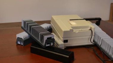 Yandan görünen antika beyaz slayt projektörü, yukarıdan slaytlar saçılmış, projektörün ışığı beyaz duvara yansıtılmış., 