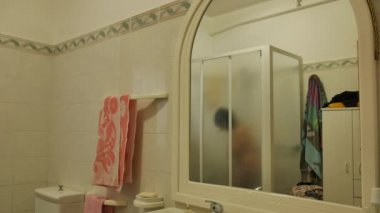 Banyoda, duşta, duşta, aynanın içinden tamamen sisli bir şekilde görülen bir kadının zaman aşımı.