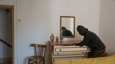 home burglary, a thief who enters an apartment through a closed window, opens the windows. thief dressed in black with balaclava.
