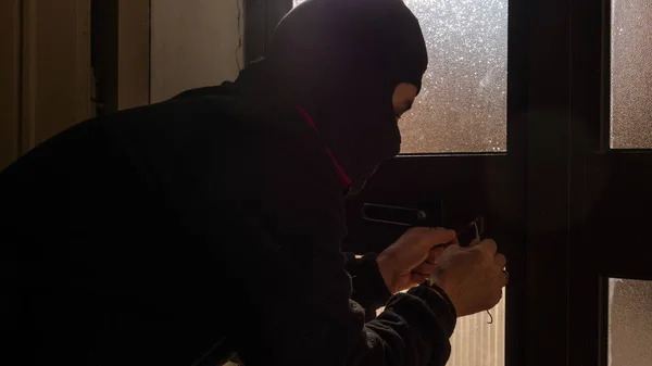 Home burglary, a thief who enters an apartment through a closed window, opens the windows. thief dressed in black with balaclava. — Stockfoto