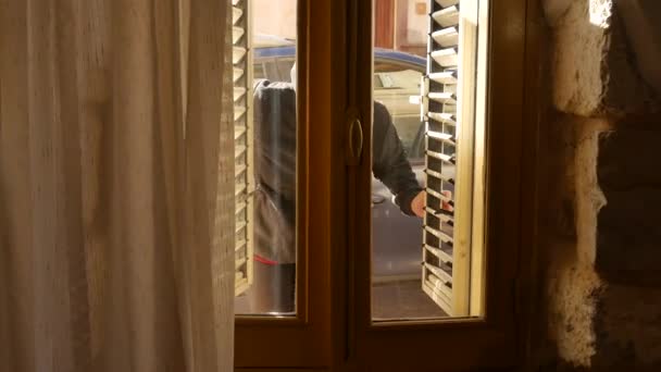 Home burglary, a thief who enters an apartment through a closed window, opens the windows. thief dressed in black with balaclava. — Vídeo de stock