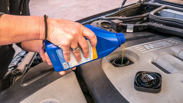 Ajouté de l'huile moteur embouteillée directement dans le compartiment moteur. mécanicien en ajoutant de l'huile moteur sur un bmw 320 diesel. huile nouvelle. Images De Stock Libres De Droits