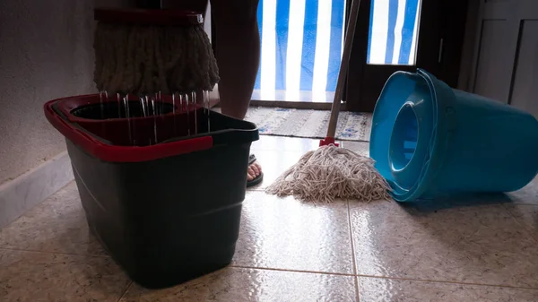 Mopp som vrir seg i bøtta, klar til å vaske gulvet med fliser og fargerike gardiner på døren i bakgrunnen.. – stockfoto