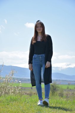 Dağlarda poz veren mavi gömlekli ve kot pantolonlu genç bir kadın.