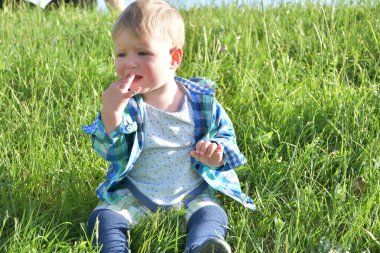 Çocuk çimenlerde oturuyor.,