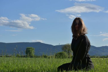 Siyah elbiseli bir kız çimlerin üzerinde oturuyor.,