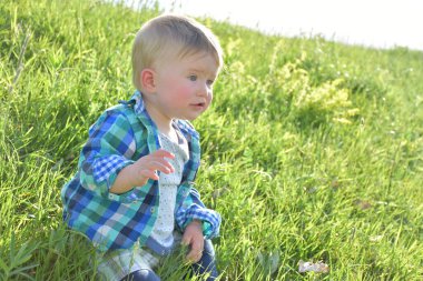 Çocuk çimenlerde oturuyor.,