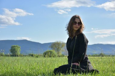 Siyah elbiseli bir kız çimlerin üzerinde oturuyor.,