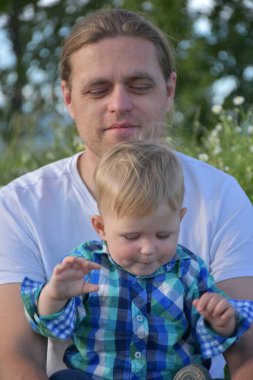 Baba ve oğul çimenlerde ve papatyalarda oturuyorlar.,