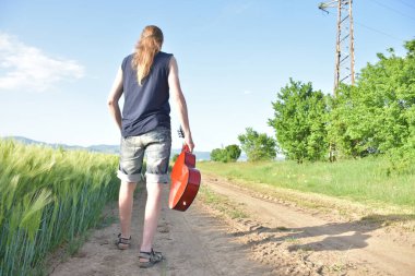 Yeşil buğday tarlası ve gitarlı bir adam.,