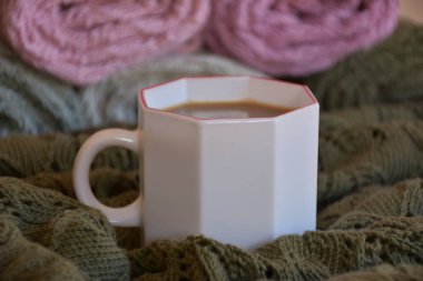 Arka planda çok renkli battaniyelerle servis edilen beyaz bir fincan kahve.