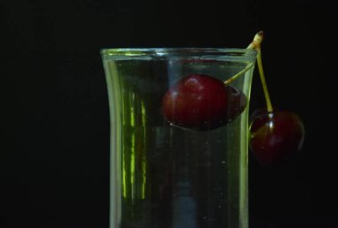 Koyu arkaplanda cam kaplı kirazlı içecek.