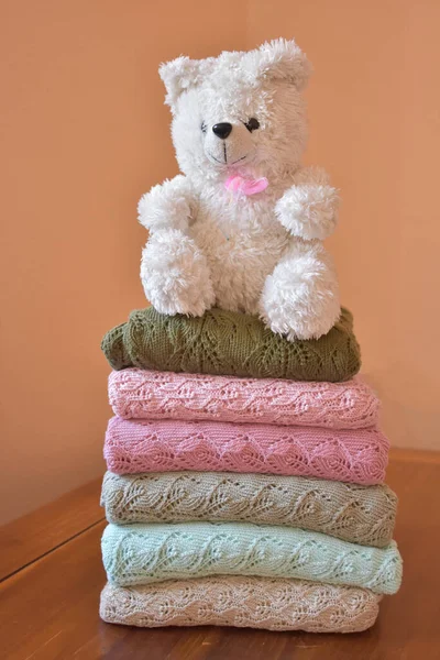 Cute teddy bear toy put on stacked knitted clothes