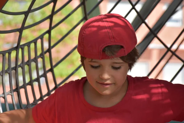 Boy in red cap playing outside on playground with net background