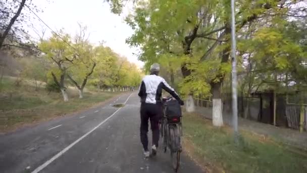 Starszy mężczyzna rasy kaukaskiej z rowerem spacerujący po jesiennej drodze — Wideo stockowe