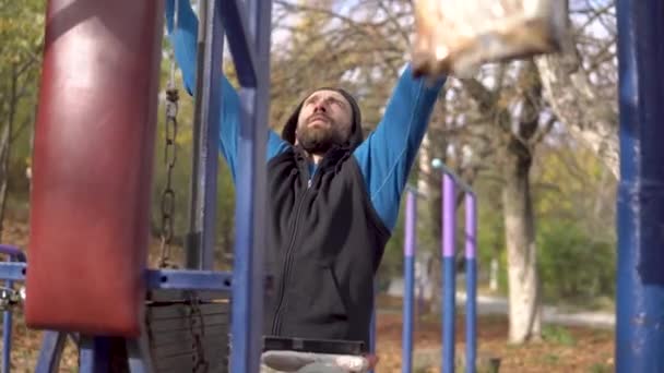 Strong Grey-Haired Man With Dreadlocks ejercitando con un aparato de entrenamiento en Open Air Gym en otoño. Bajando un peso. Entrenamiento callejero de la ciudad — Vídeo de stock