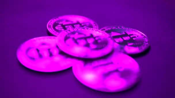 Цифровая монета Bitcoin вращается с другой биткоинами на чёрной поверхности. Фиолетовый неоновый свет — стоковое видео