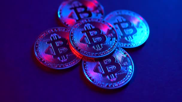 Moneda digital Bitcoin gira con otro Bitcoins en la superficie negra. Luz de neón rosa y azul — Vídeo de stock