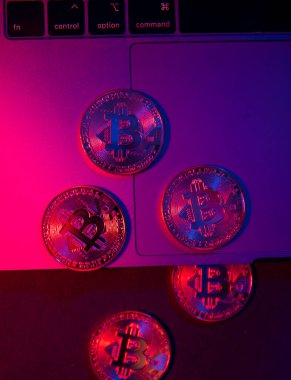 Bitcoin 'in paraları dizüstü bilgisayarın yüzeyinde. Mor ve pembe neon ışık