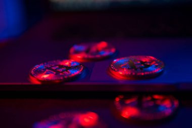 Bitcoin 'in paraları dizüstü bilgisayarın yüzeyinde. Mor ve pembe neon ışık