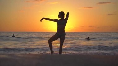 Gün batımında plajda mayo giymiş zarif Asyalı kız dans ediyor. Puerto Escondido 'da okyanus batımı. Yavaş Hareket HD