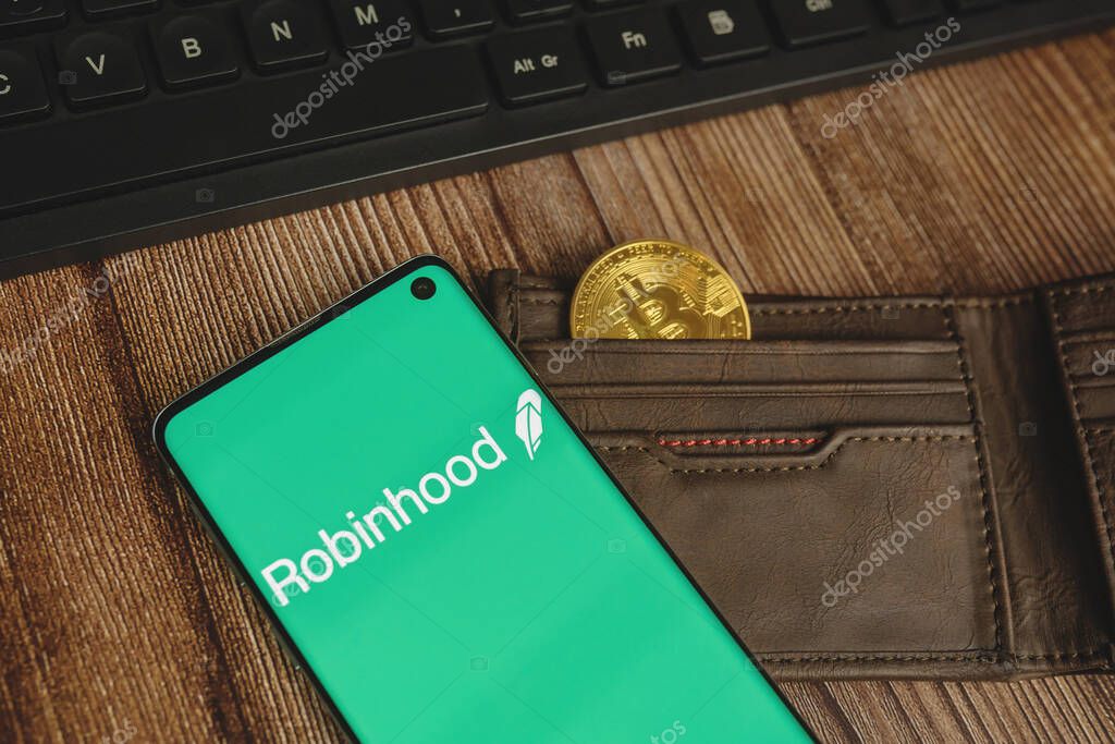 WARSAW, POLAND - FEBRUARY 17, 2021: Robinhood app green logo with gold Bitcoin in a brown waller and keyboard on wood backround
