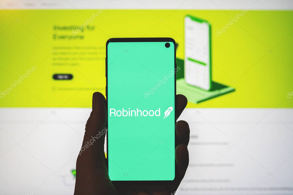 Robinhoodapp logo on smartphone in hand with blurred website background. American financial service, cryptocurrency exchange platform. Swansea, UK - July 31, 2021