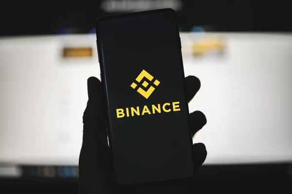 Значок Binance на телефоне с официальным фоном сайта — стоковое фото