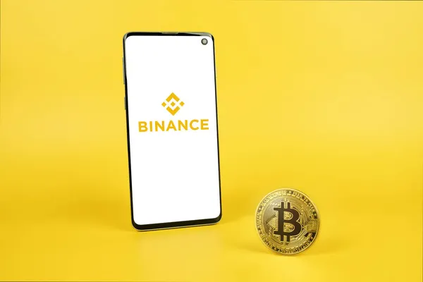 Логотип Binance на смартфоне и Bitcoin на желтом фоне — стоковое фото