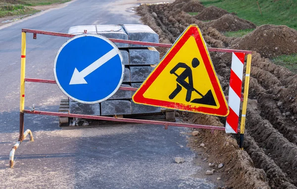 İnşaat üçgeni yol işareti ve mavi ok işareti altında.