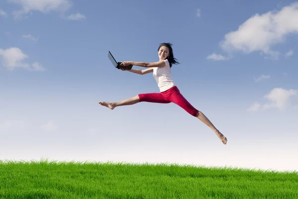 Woman with laptop jumping in meadow — Stock Photo, Image
