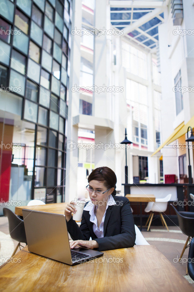 Business woman typing on laptop while having coffee