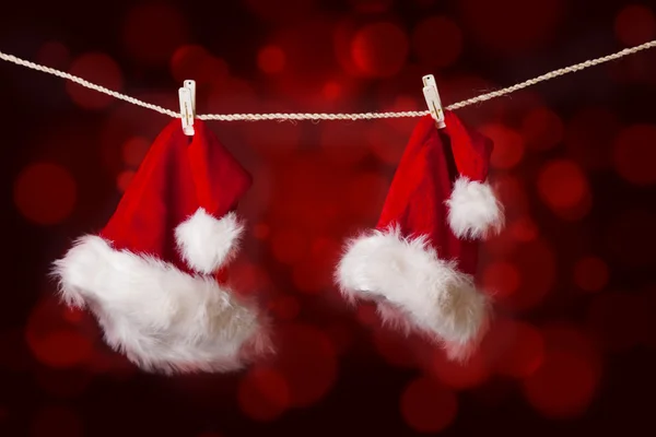 Dois chapéus de Natal Papai Noel pendurados em luzes desfocadas vermelhas — Fotografia de Stock