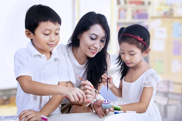 Glad lärare och förskolebarn måla påskägg — Stockfoto