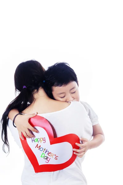 Menino abraço mãe segurando cartão de amor no branco — Fotografia de Stock