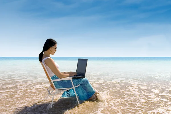 Attraktive Frau tippt am Strand auf Laptop — Stockfoto