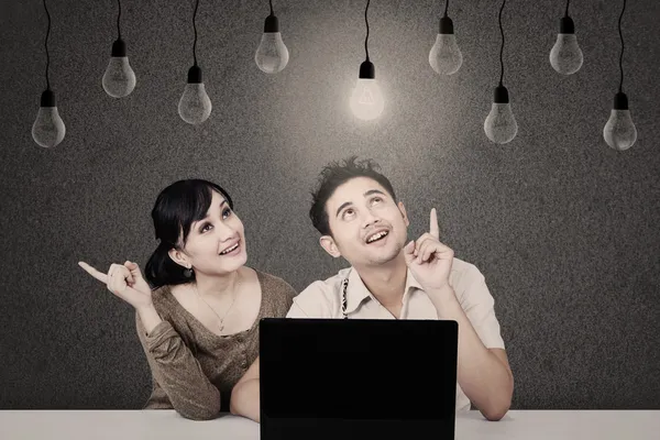 Casal com laptop olhando para lâmpada acesa — Fotografia de Stock