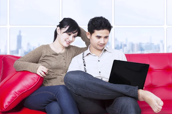 Para szuka na laptopie w mieszkaniu na czerwonej kanapie — Zdjęcie stockowe